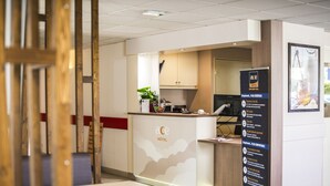 A hotel reception area with a modern design, including a reception desk, a digital screen, and a menu board. - Ace Hotel Clermont-Ferrand La Pardieu (Clermont-Ferrand)