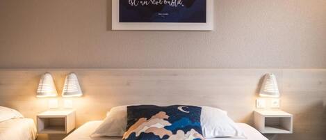 A hotel room with a bed, two bedside lamps, a night sky-themed pillow, and a framed quote on the wall.