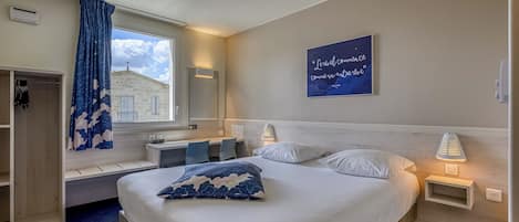 Habitación de hotel con cama, mesitas de noche, ventana con vistas, un banco empotrado y una obra de arte en la pared.