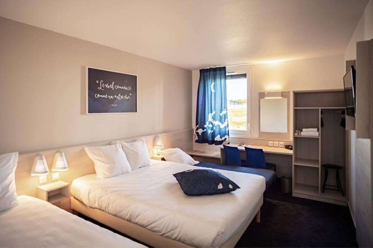 A hotel room with two beds, a desk, a chair, a wardrobe, and a television.