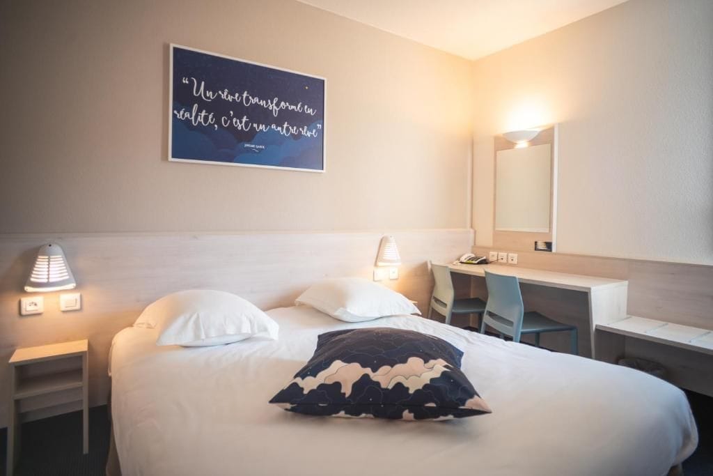 A hotel room with a bed, bedside lamps, a desk, and a mirror.