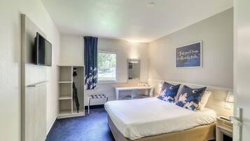 A hotel room with a bed, a desk, a chair, a mirror, and a TV.