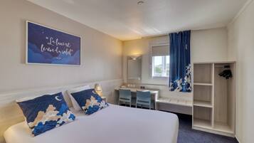 A hotel room with a bed, desk, chair, wardrobe, and a night sky-themed wall decoration.