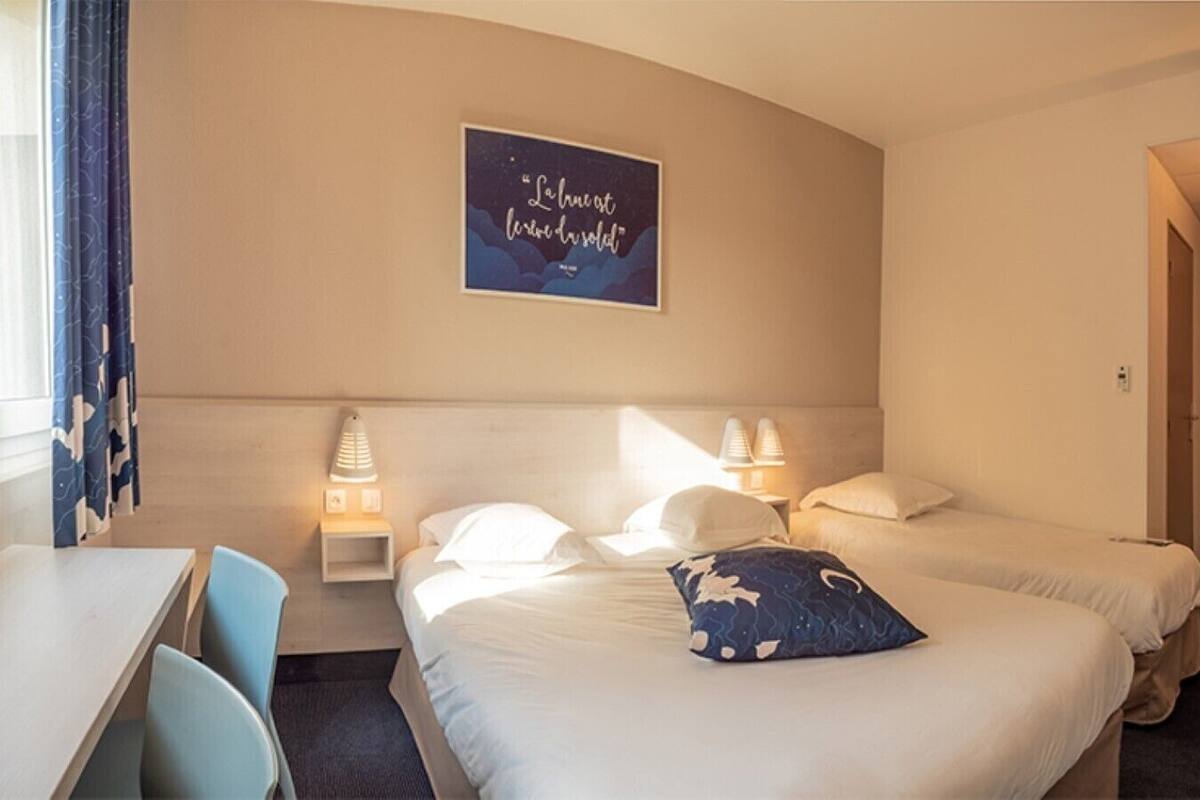 A hotel room with two beds, a desk, chairs, and a wall-mounted artwork.