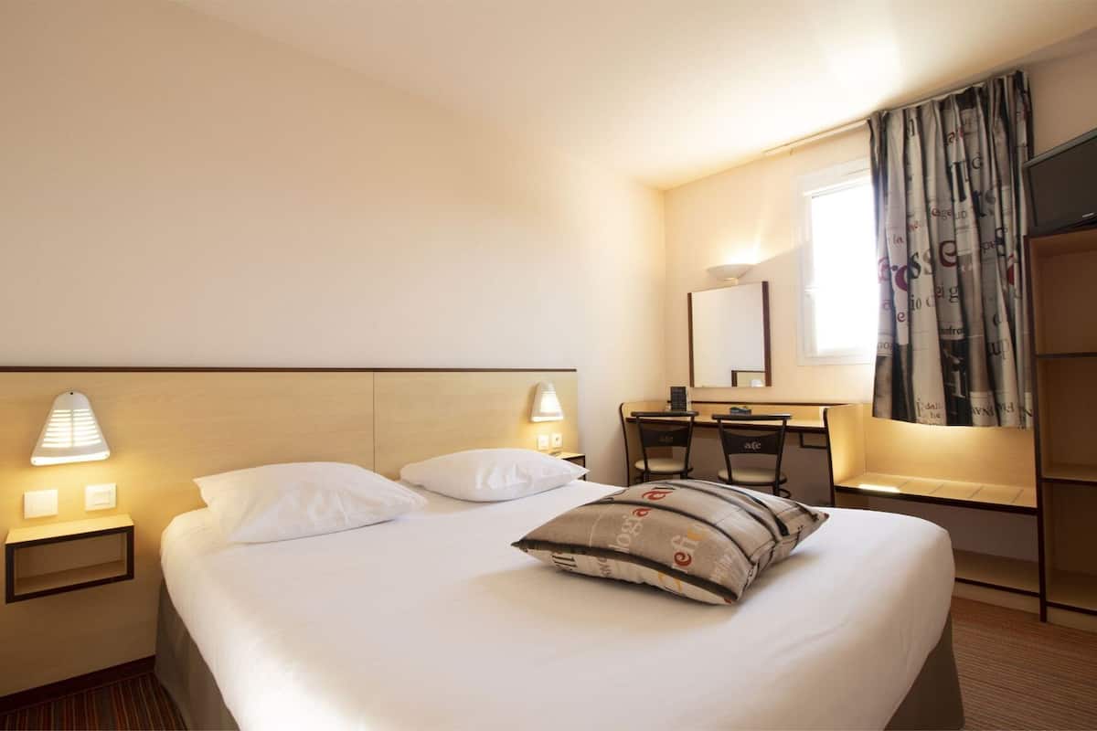 A hotel room with a bed, bedside lamps, a desk, a chair, a mirror, and a wardrobe.