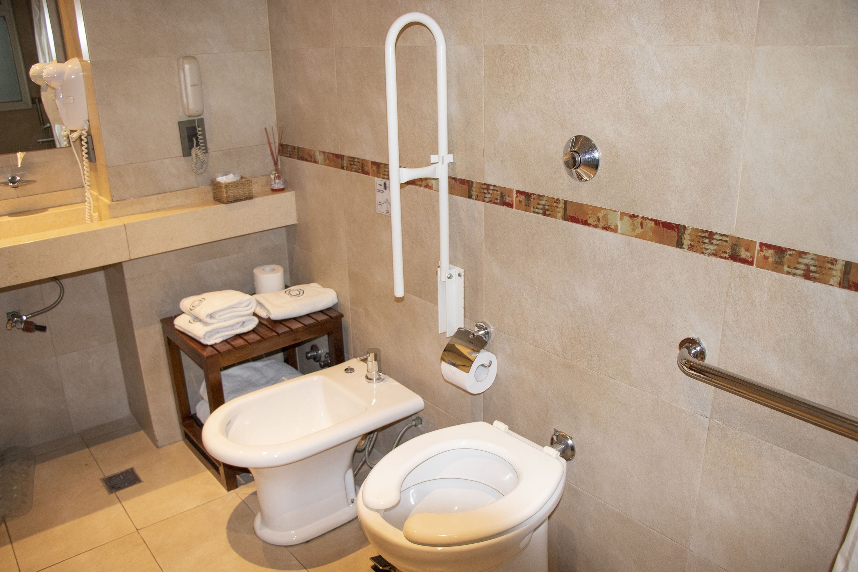 A bathroom with a toilet, bidet, and a handrail.