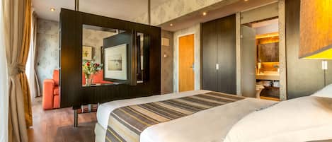 Habitación de hotel moderna con una cama grande, televisión, espejo y baño visible a través de una puerta abierta.