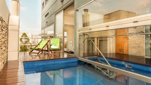 Una piscina interior con muelle de madera, paredes de cristal y vistas a la ciudad.