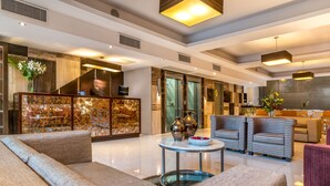 Un lobby espacioso con diseño moderno, que incluye una zona de estar con sofás y sillones, una mesa redonda con objetos decorativos y un mostrador de recepción con un gabinete decorativo.