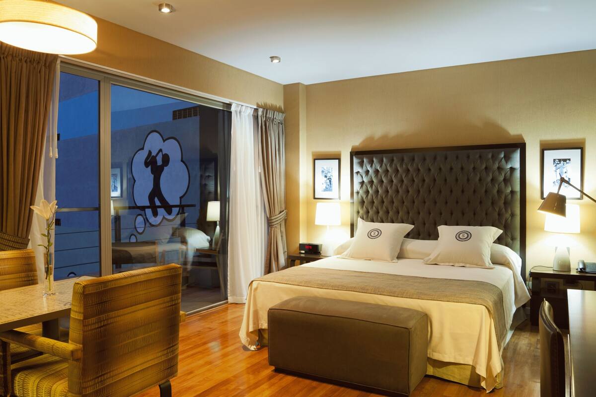 Habitación de hotel con una cama grande, una mesa de comedor y vistas al exterior.