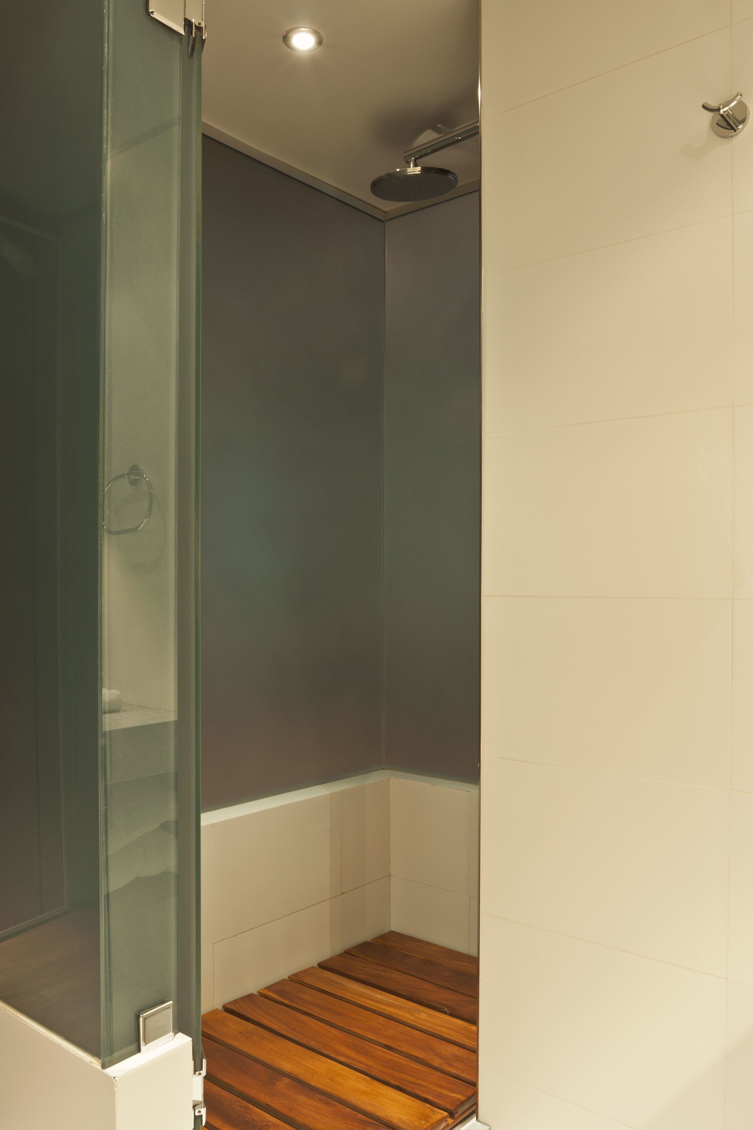 A bathroom with a glass shower enclosure, wooden flooring, and white walls.