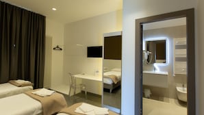 Une chambre d’hôtel avec deux lits, un bureau, une chaise, un miroir et une salle de bain équipée d’un lavabo et d’une douche.