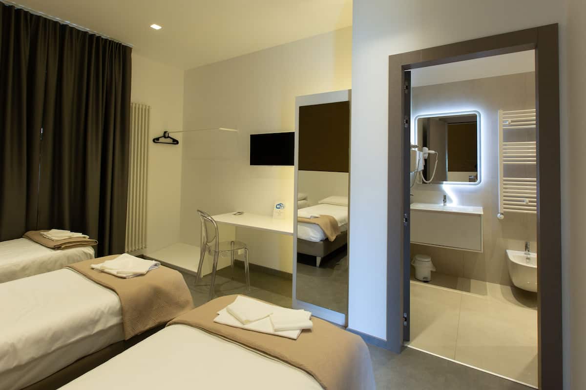 Et hotelværelse med to senge, et skrivebord, en stol, et spejl og et badeværelse med håndvask og brusebad.