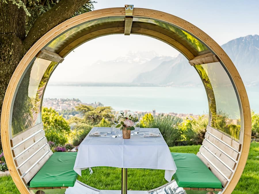 Una estructura circular de madera con una mesa y bancos, con vistas a un lago y montañas.