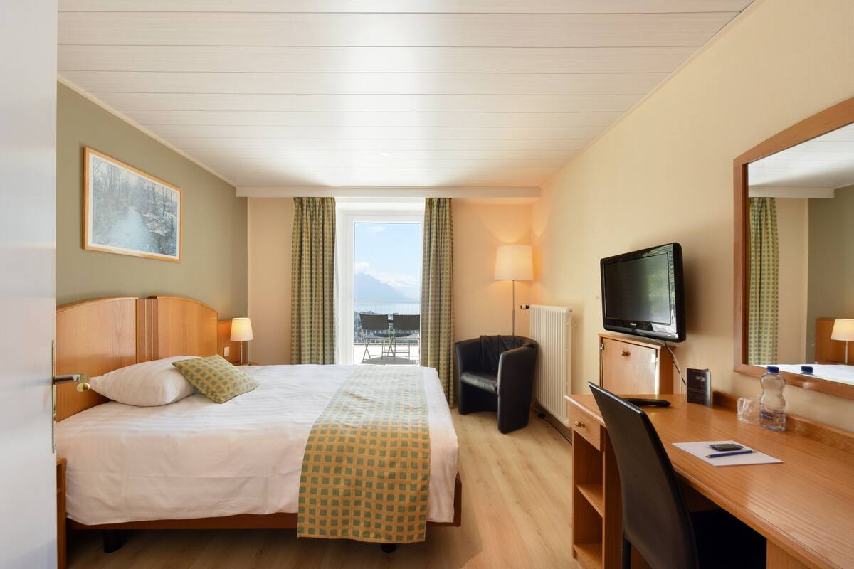 A hotel room with a bed, desk, chair, television, and a view of the outdoors.