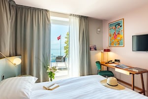 Quarto de hotel com cama, escrivaninha, cadeira, televisão e varanda com uma bandeira.