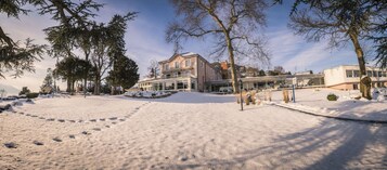 Paisagem coberta de neve com um prédio grande com varanda e uma construção moderna próxima.