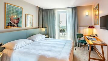 A hotel room with a large bed, a desk, a chair, and a balcony with a view.