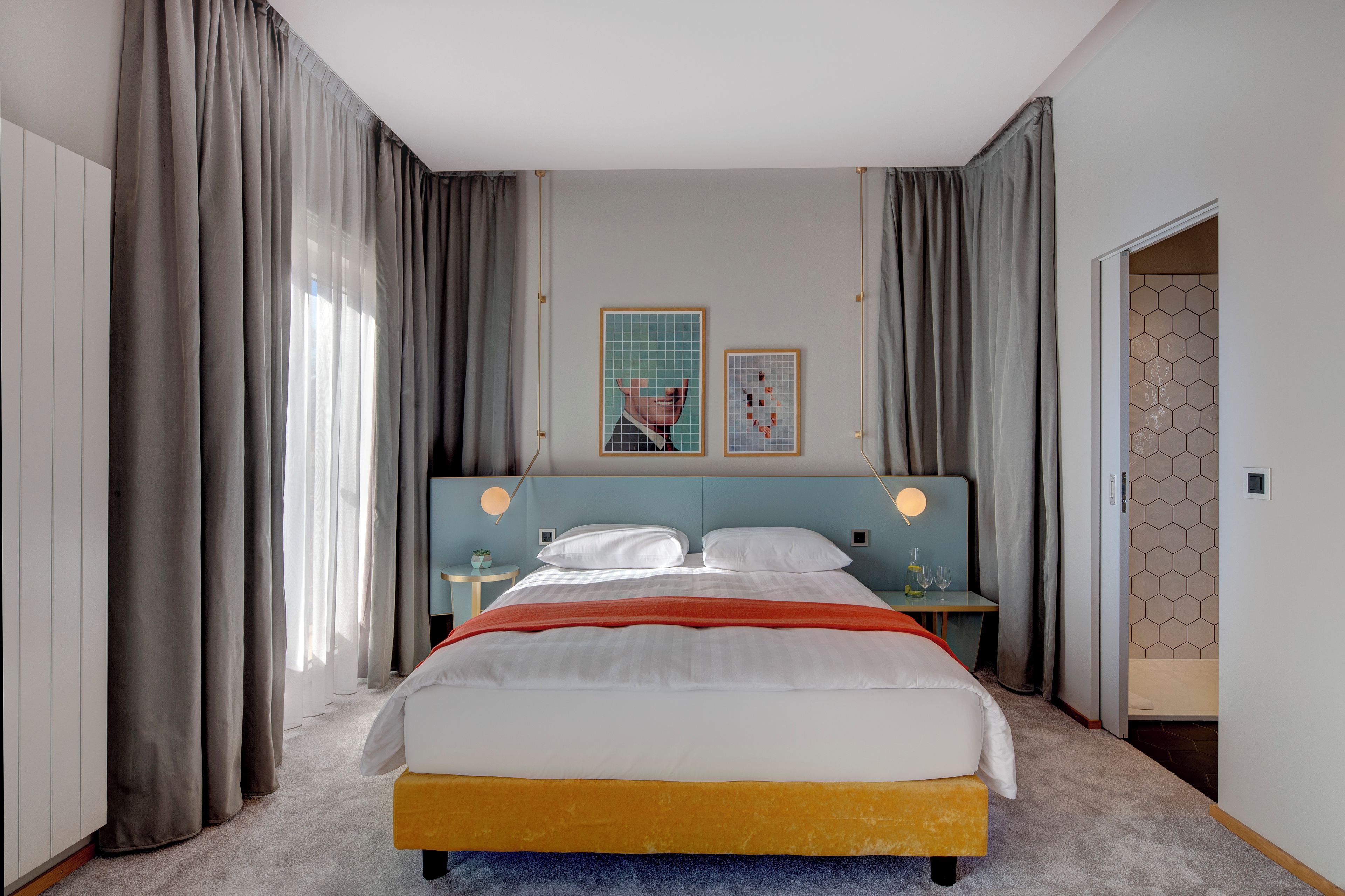 Un dormitorio moderno con cama, cortinas, cabecero, mesitas de noche y una obra de arte en la pared.