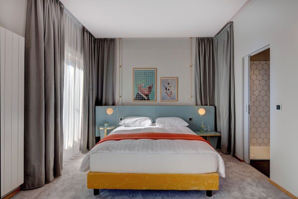 Un dormitorio moderno con cama, cortinas, cabecero, mesitas de noche y una obra de arte en la pared.