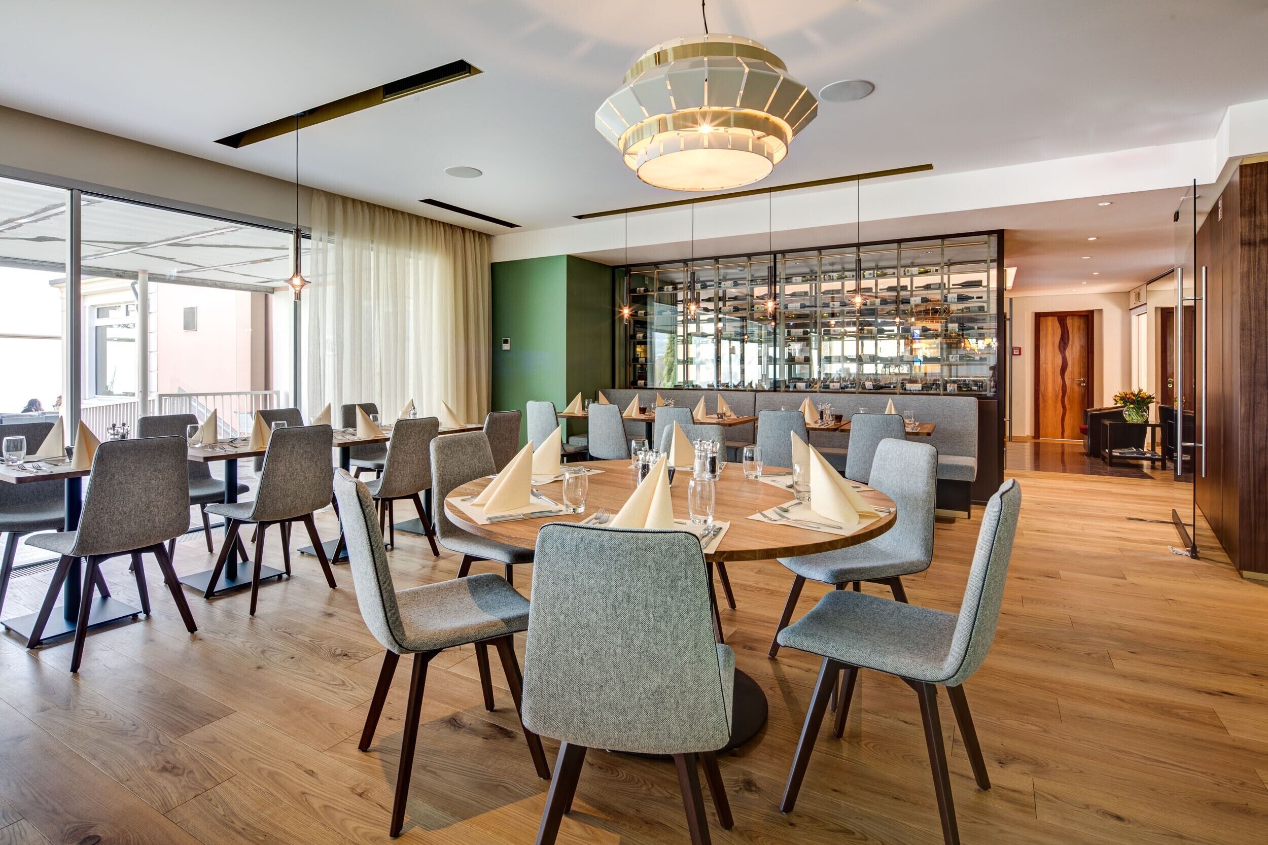 Un comedor moderno con mesas redondas, sillas tapizadas en gris y un lámpara central.
