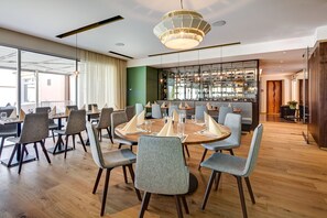 A modern dining area with round tables, grey upholstered chairs, and a central light fixture. - Hotel du Leman (Jongny)