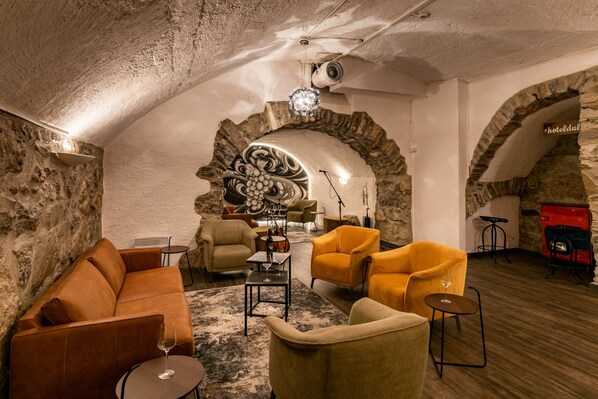 Un salón acogedor con paredes de piedra, piso de madera y una mezcla de muebles modernos y antiguos, incluyendo un sofá, sillones y una pequeña mesa con una copa de vino.