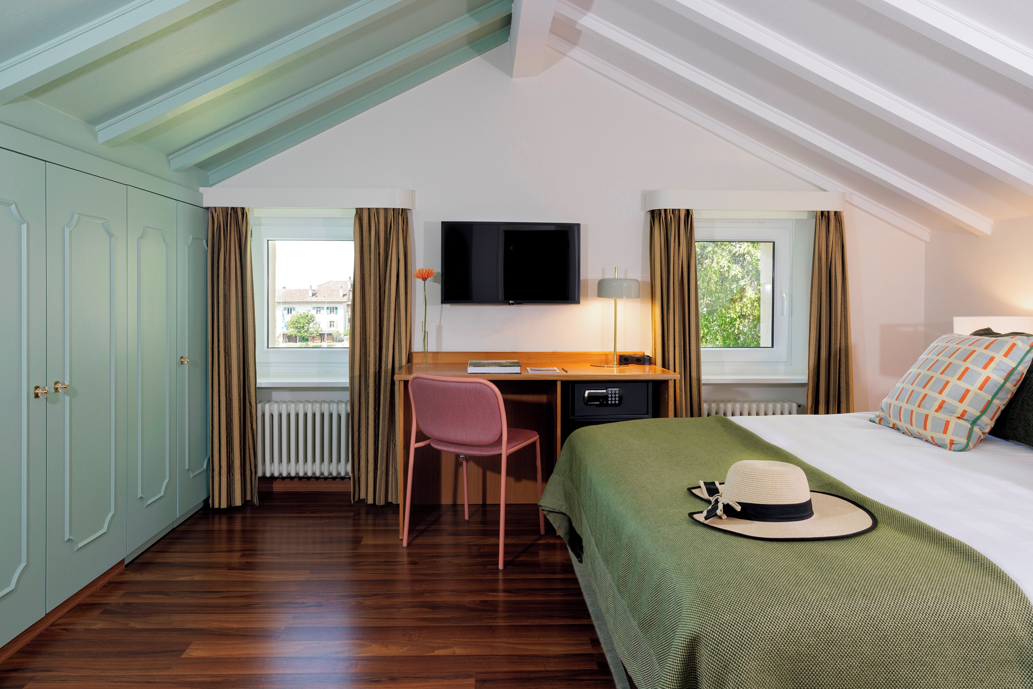 Una camera d'albergo con un letto, una scrivania, una sedia, una televisione e una finestra.