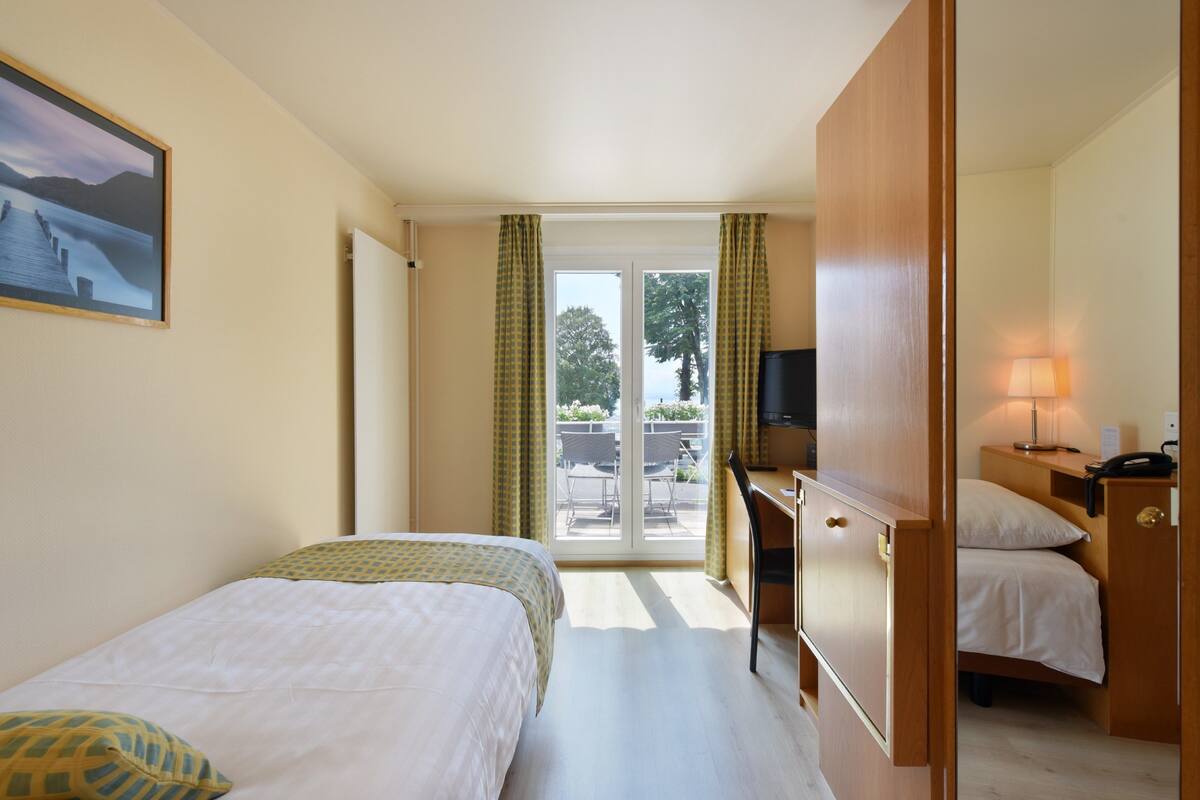 A hotel room with a bed, a desk, a chair, a television, and a view of the outdoors.