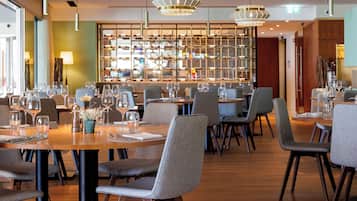 A restaurant with multiple tables, chairs, and hanging pendant lights.