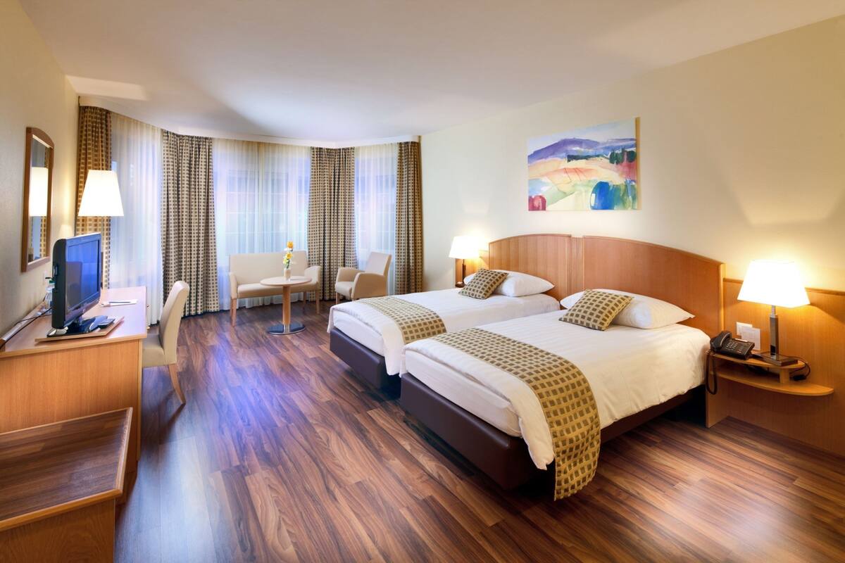 A hotel room with two beds, a desk with a computer, a chair, and a TV.
