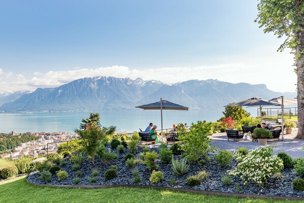 Una terraza con mesas al aire libre, vista a un lago y montañas al fondo.