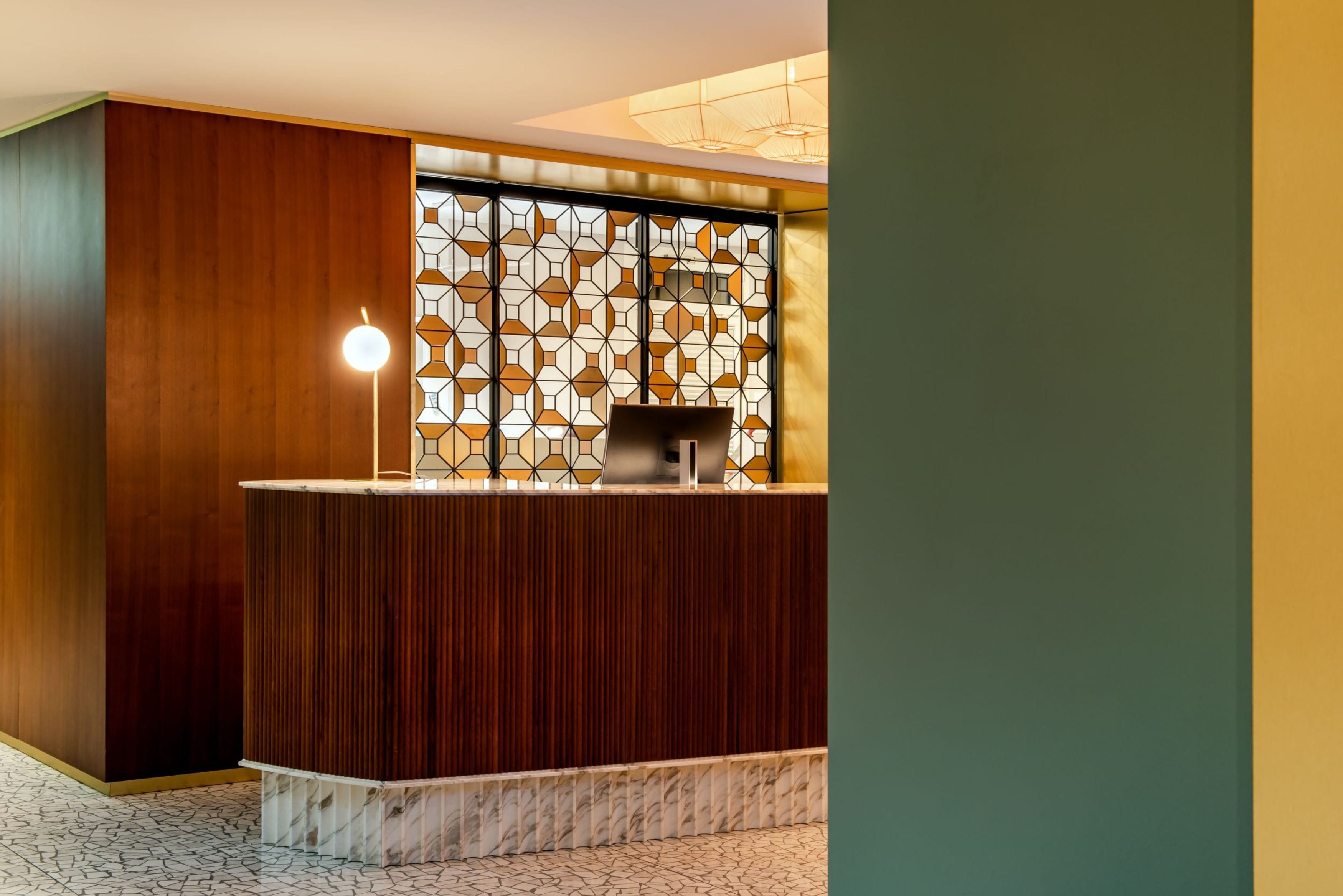 A reception area with a wooden reception desk, a patterned glass partition, and a floor with a geometric tile pattern.