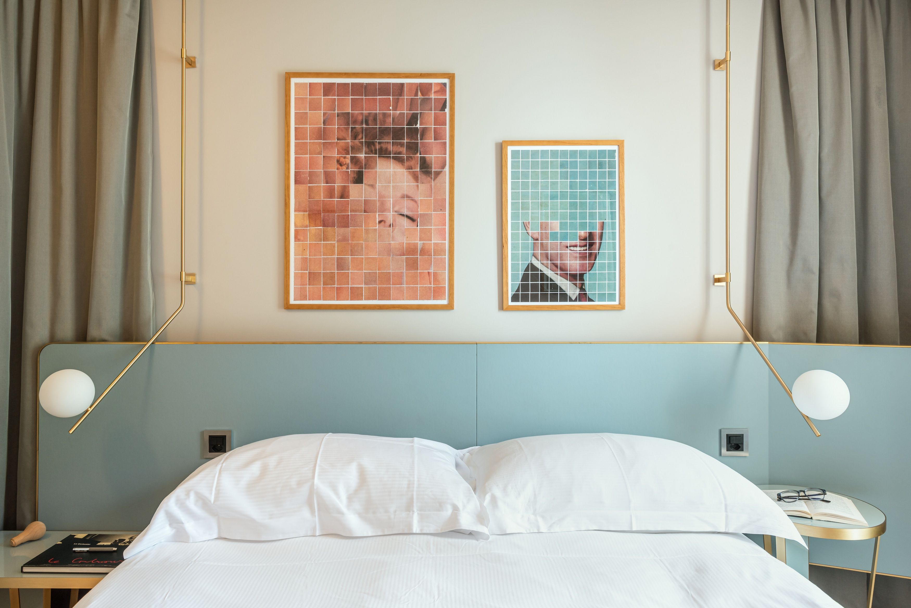 A bed with white linens, a nightstand with a book and a pen, and two framed pictures on the wall.