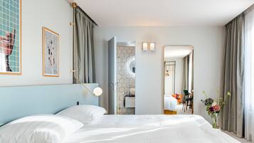 Habitación de hotel con una cama grande, un baño con pared de azulejos hexagonales y vista al interior de la habitación.