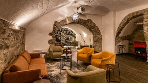 A cozy lounge with stone walls, a wooden floor, and a mix of modern and vintage furniture including a sofa, armchairs, and a small table with a wine glass. - Hotel du Leman (Jongny)