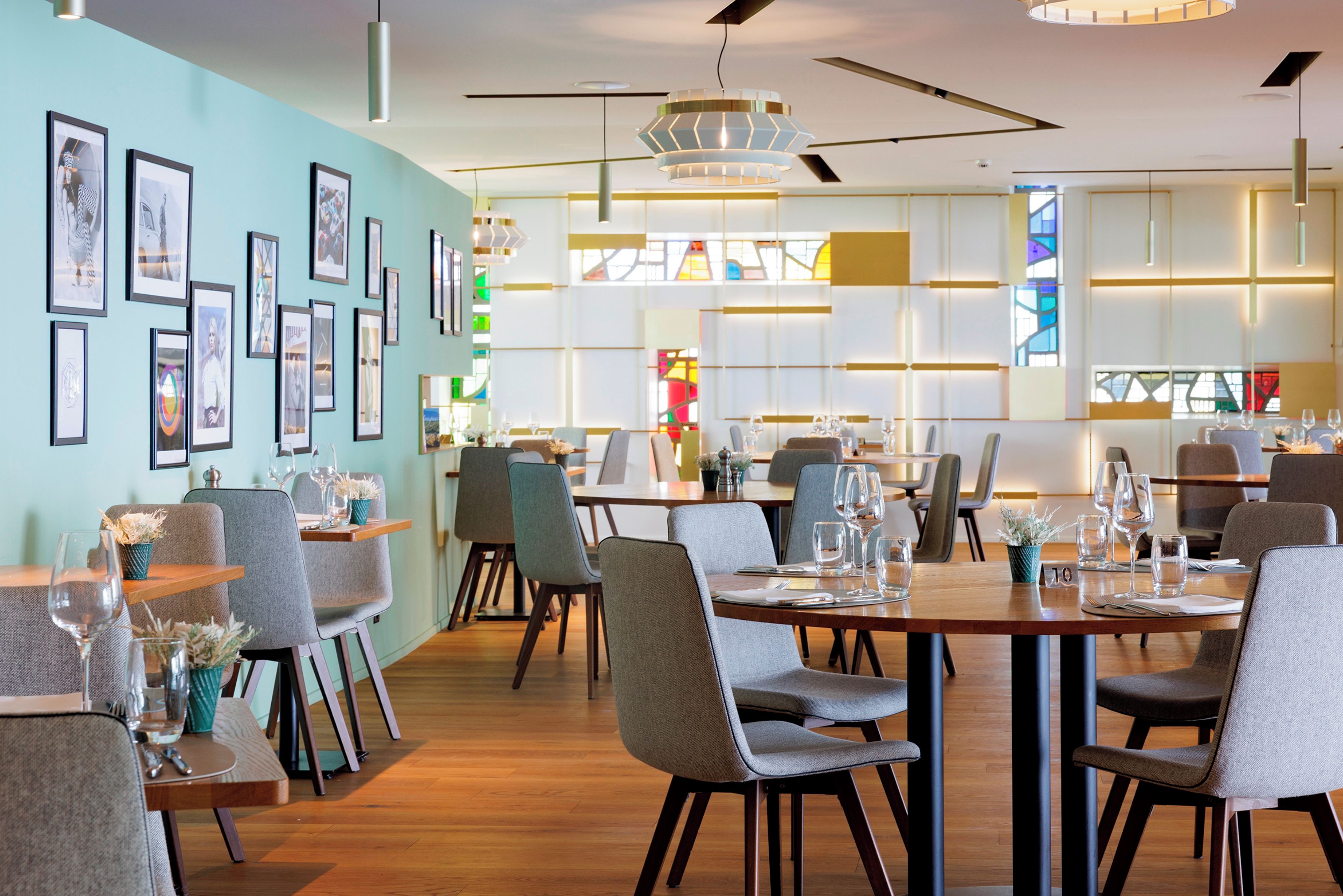 A modern dining area with wooden tables, grey upholstered chairs, and framed artwork on the walls.