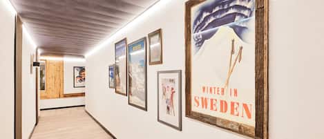 A hallway with framed pictures on the walls, a wooden floor, and a ceiling with a grid pattern.
