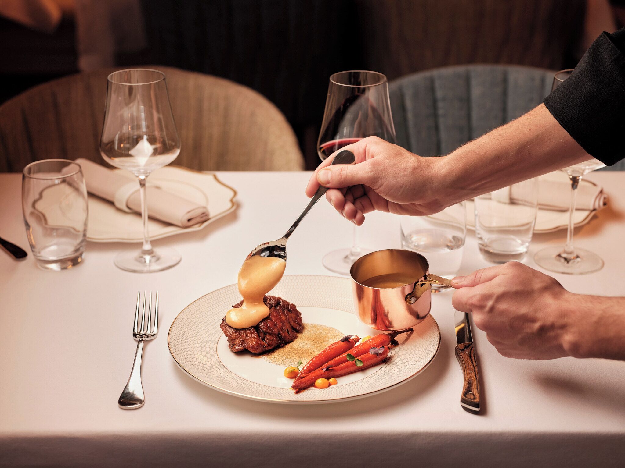 A dining table with a plate of food, a spoon, and a wine glass.