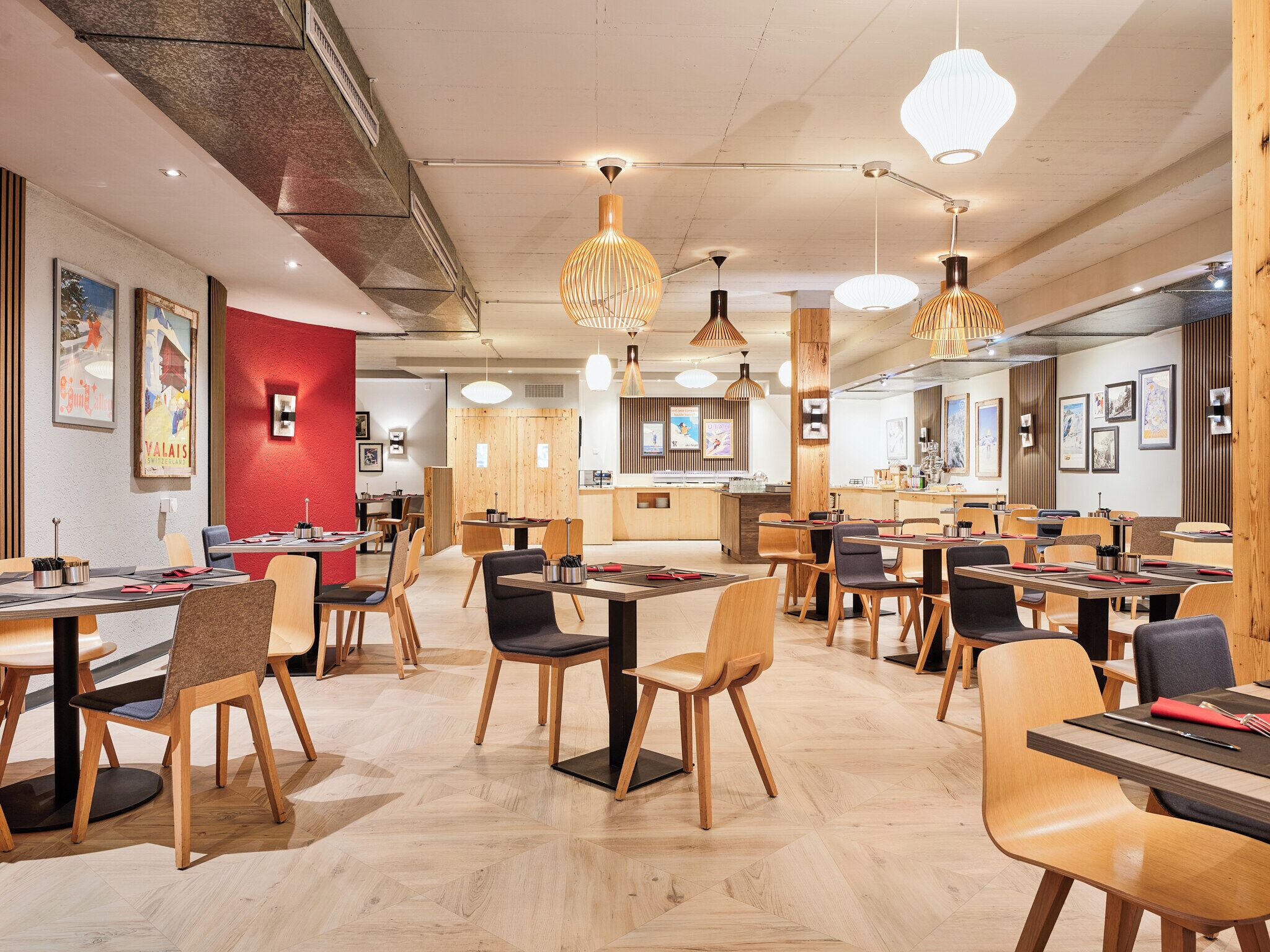 A modern restaurant interior with wooden furniture, pendant lighting, and artwork on the walls.