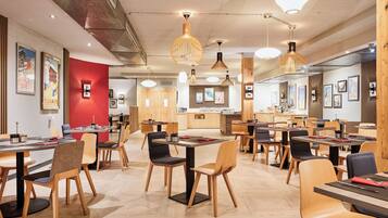 A modern restaurant interior with wooden furniture, pendant lighting, and artwork on the walls.