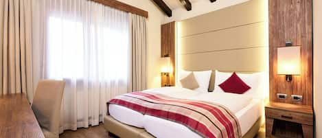 A hotel room with a large bed, wooden headboard, bedside tables with lamps, a wooden desk, and a chair.