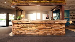 A reception area with a stone and wood counter, a potted plant, and a view of the outdoors. - Hotel Ambassador Zermatt (Zermatt)