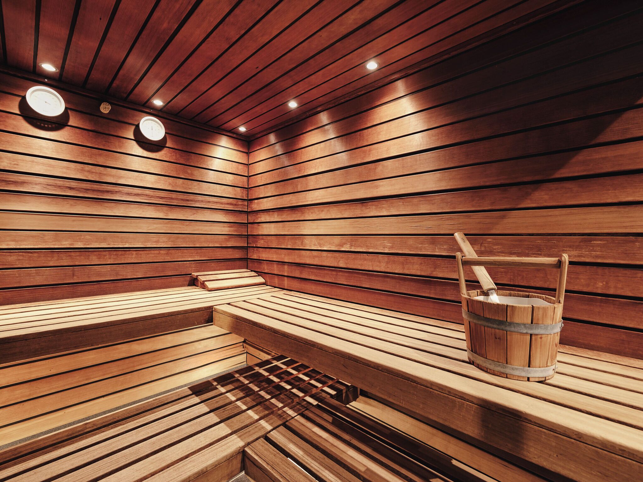 A sauna with wooden benches and a wooden bucket.