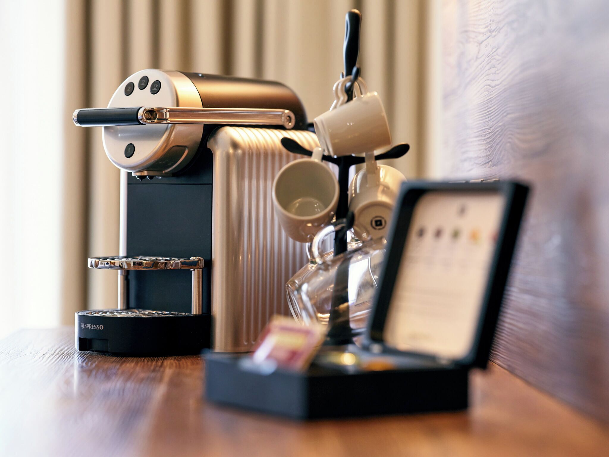 A coffee machine with a digital display, a coffee cup, and a Nespresso pod holder on a wooden surface.