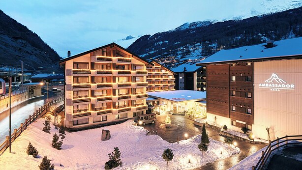 A hotel with multiple balconies, a snow-covered courtyard, and a mountain backdrop. - Hotel Ambassador Zermatt (Zermatt)