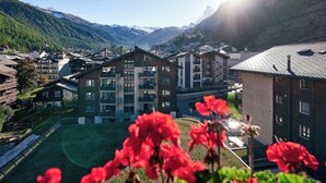 A mountain resort with multiple buildings, including a prominent lodge with balconies, set against a backdrop of snow-capped mountains and lush greenery. - Hotel Ambassador Zermatt (Zermatt)