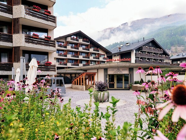 Ein Hotel mit mehreren Balkonen, einem zentralen Eingang und einer Bergkulisse.