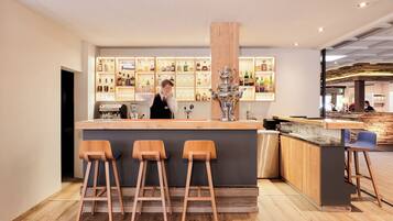 A bar area with a wooden counter, stools, and shelves of bottles.