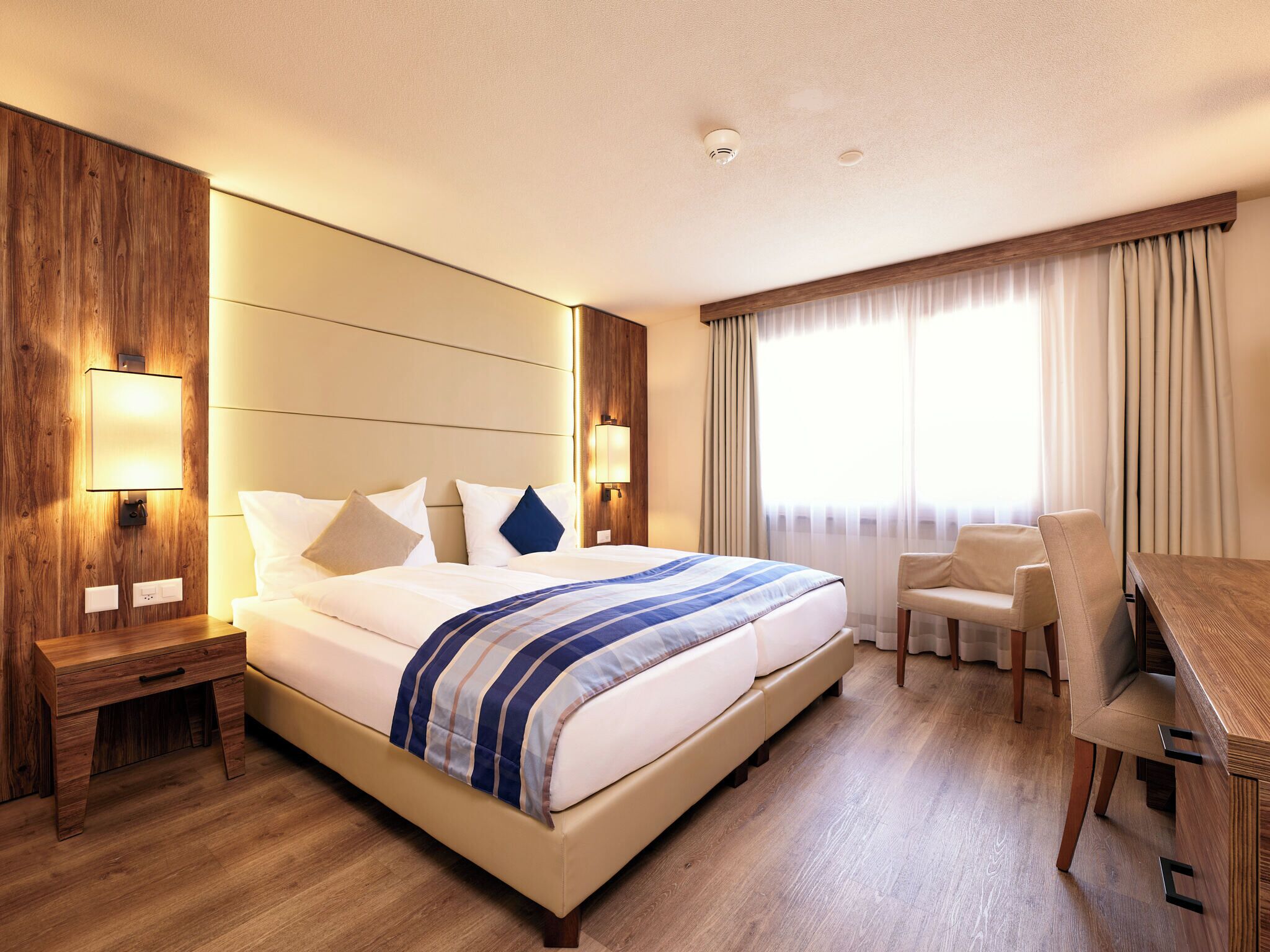 Una habitación de hotel con una cama grande, mesitas de noche, un escritorio y una silla.